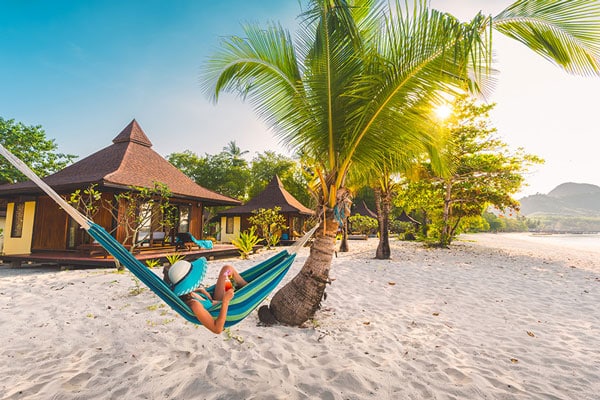 Eine Frau in einer Hängematte am Strand vor dem Sivalai Beach Resort auf Koh Mook.