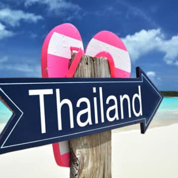 Schild mit dem Schriftzug Thailand an einem thailändischen Strand, mit Flip Flops.