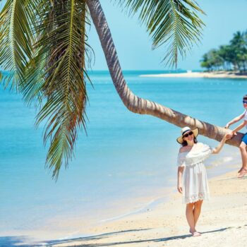 Mutter und kleiner Sohn am tropischen Strand sitzen auf einer Palme im Sommer Urlaub auf Koh Samui