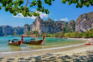 Strand von Raily, bei Krabi in Thailand mit einem typischen Longtailboot und badenden Touristen