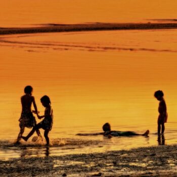 Kinder die bei Dämmerung am Meer spielen auf der Insel Koh Samui in Thailand.