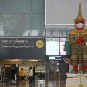 Eine thailaendische Statue am Flughafen Bangkok mit einer Maske vor dem Mund.