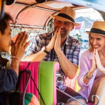 Touristen die in einem Tuk Tuk durch einen thailändischen Wai vom Fahrer begrüßt werden.