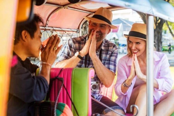 Touristen die in einem Tuk Tuk durch einen thailändischen Wai vom Fahrer begrüßt werden.