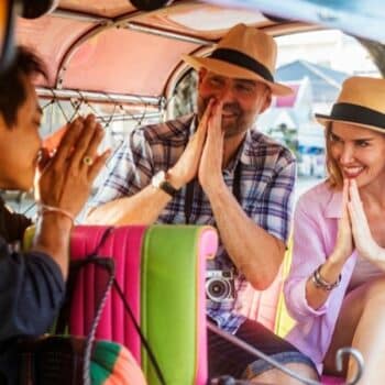 Touristen die von einem Tuk Tuk Fahrer mit dem thailändischen Wai Gruß begrüßt werden.