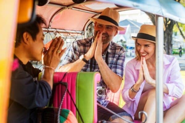 Touristen die von einem Tuk Tuk Fahrer mit dem thailändischen Wai Gruß begrüßt werden.