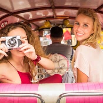 Zwei Touristen bei einer Tour mit dem Tuk Tuk durch Bangkoks Straßen.