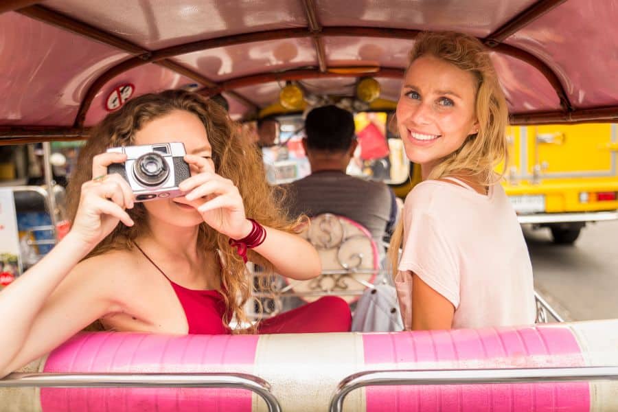 Zwei Touristen bei einer Tour mit dem Tuk Tuk durch Bangkoks Straßen.