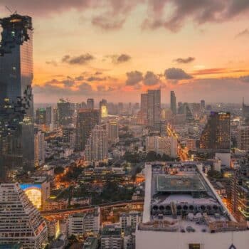 Skyline von Bangkok, einer modernen Stadt bei Sonnenuntergang mit beleuchteten Hochhäusern und einem markanten Turm im Vordergrund.