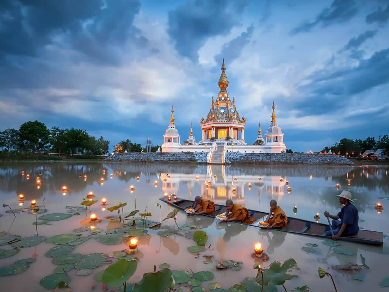 Novizen setzen Krathong-Lichter auf einem Lotussee beim Loy Krathong Fest — goldener Tempel im Spiegelbild des Abendhimmels