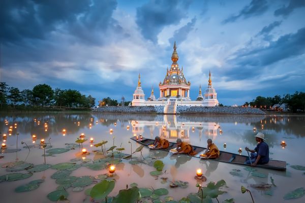 Mönche auf einem Boot lassen beim Loy-Krathong-Fest schwimmende Lichter auf einem See vor einem beleuchteten Tempel gleiten