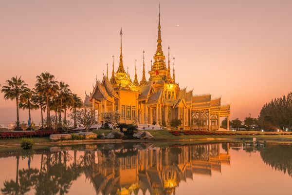 Goldener Tempel mit Palmen, der sich bei Abenddämmerung im Wasser spiegelt, Südthailand
